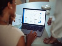 istockphoto-2161896417-612×612 Two business professionals analyzing sales data and financial charts on a laptop during a meeting in a modern office setting.